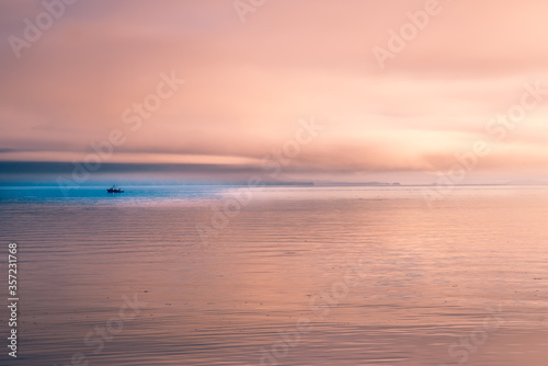 A sunset view of the coast of Alaska with a small fishing boat in the blue water