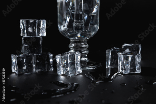 Glass decanter and stemmed glass, ice cubes, on a black background. The texture of the glass.