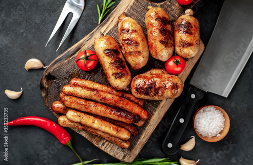 Different grilled sausages with spices and rosemary, served on a cutting board on a stone background