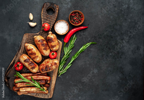 Different grilled sausages with spices and rosemary, served on a cutting board on a stone background with copy space for your text