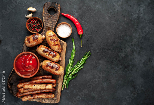 Different grilled sausages with spices and
rosemary, served on a cutting board on a stone background with copy space for your text
