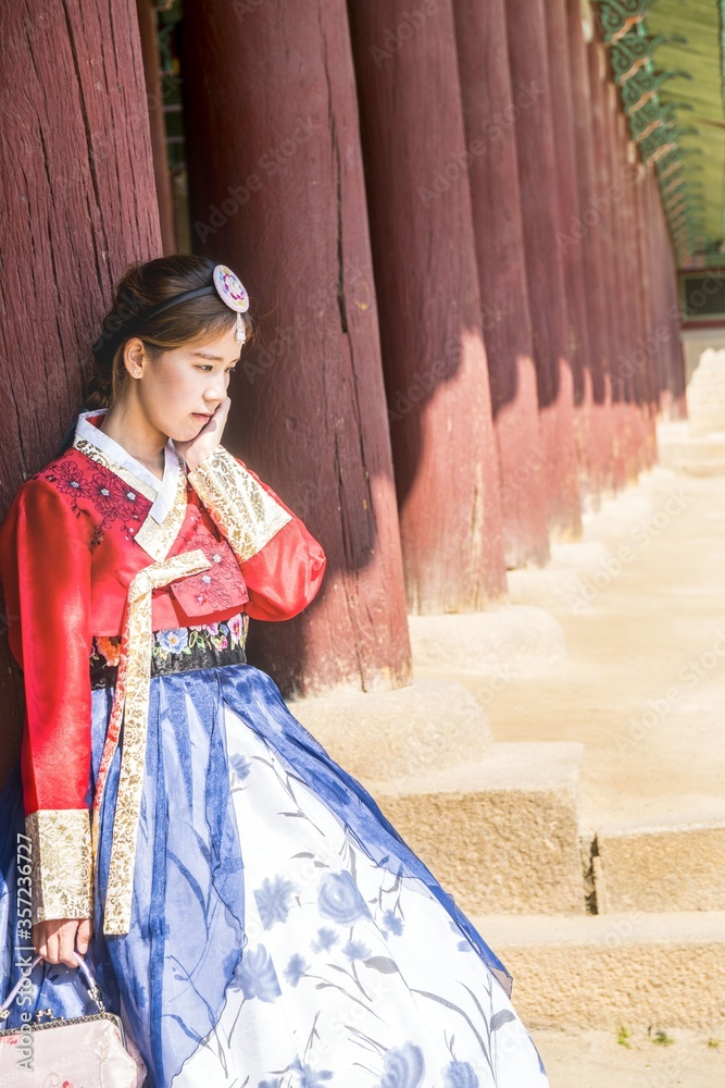 Asian woman in a traditional costume standing behind brown columns under the sun