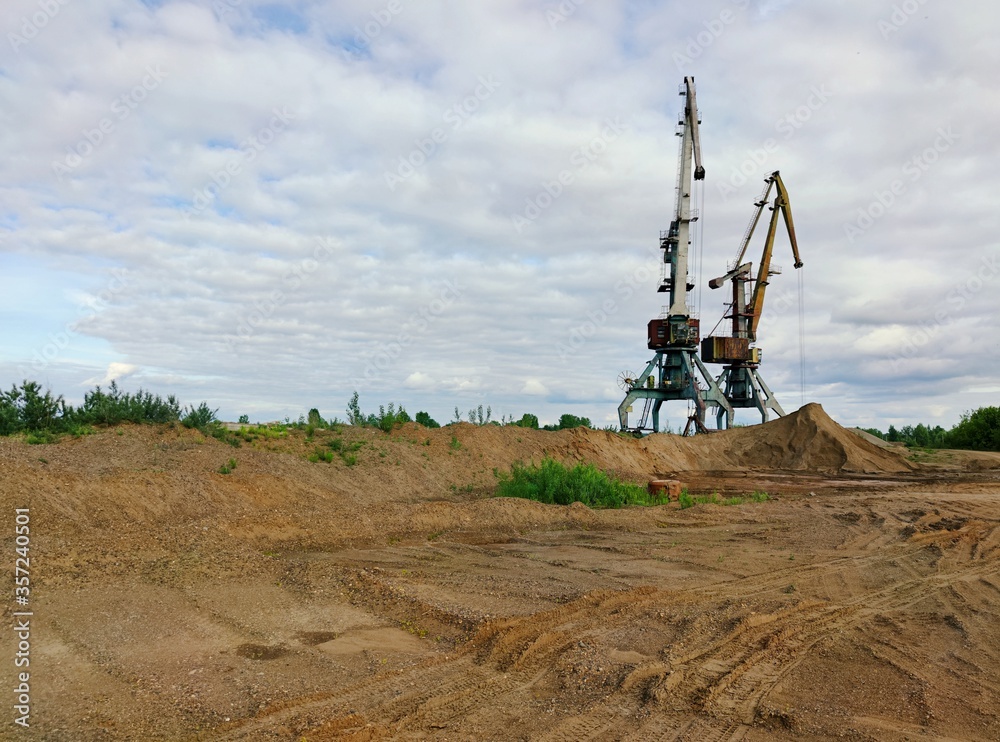 two old large cranes on a sand quarry against the evening blue cloudy sky