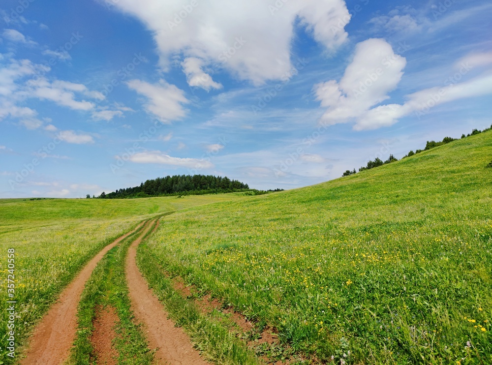 beautiful blue sky with white clouds over the road in a green field near the hillside on a sunny day beautiful blue sky with white clouds over the road in a green field near the hillside on a sunny day