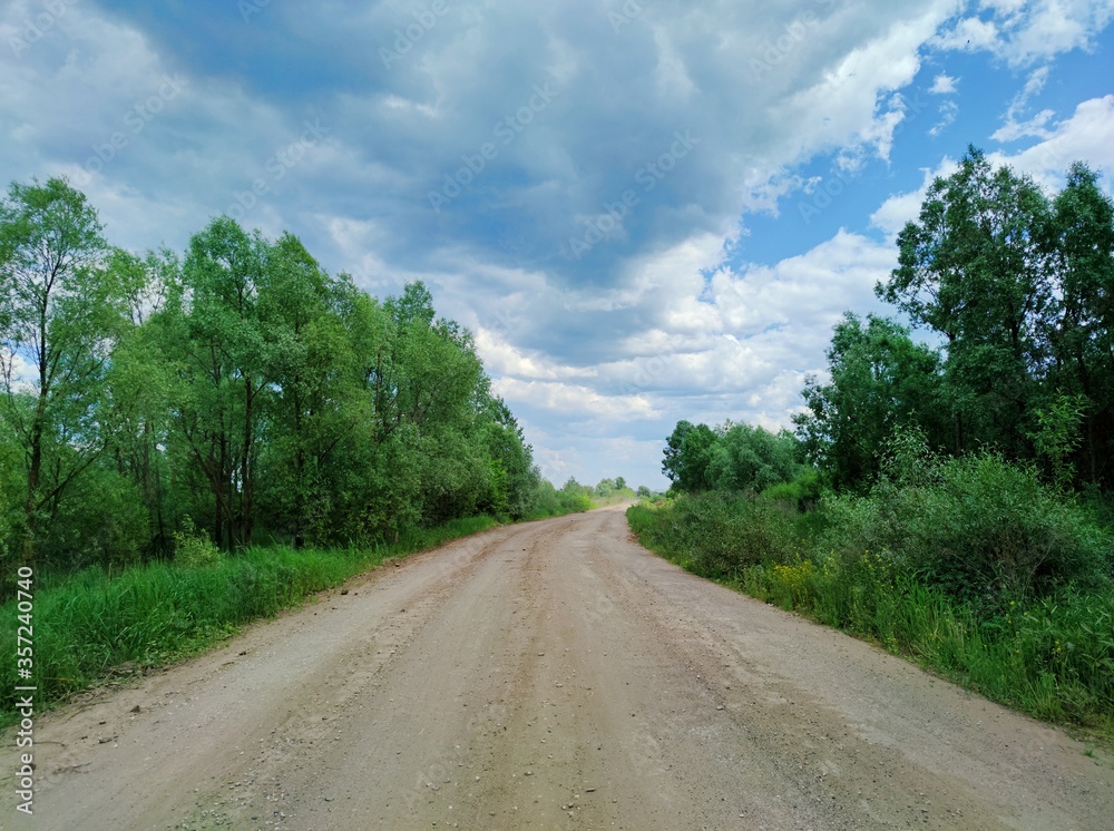 road with old jagged asphalt between trees against a blue sky with beautiful clouds on a sunny day