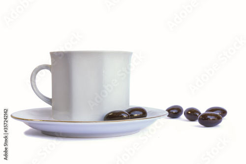 White porcelain cup on plate and chocolate candies around, isolated on white background. Tea break concept, snack, hot beverage. Luxury porcelain utensils.