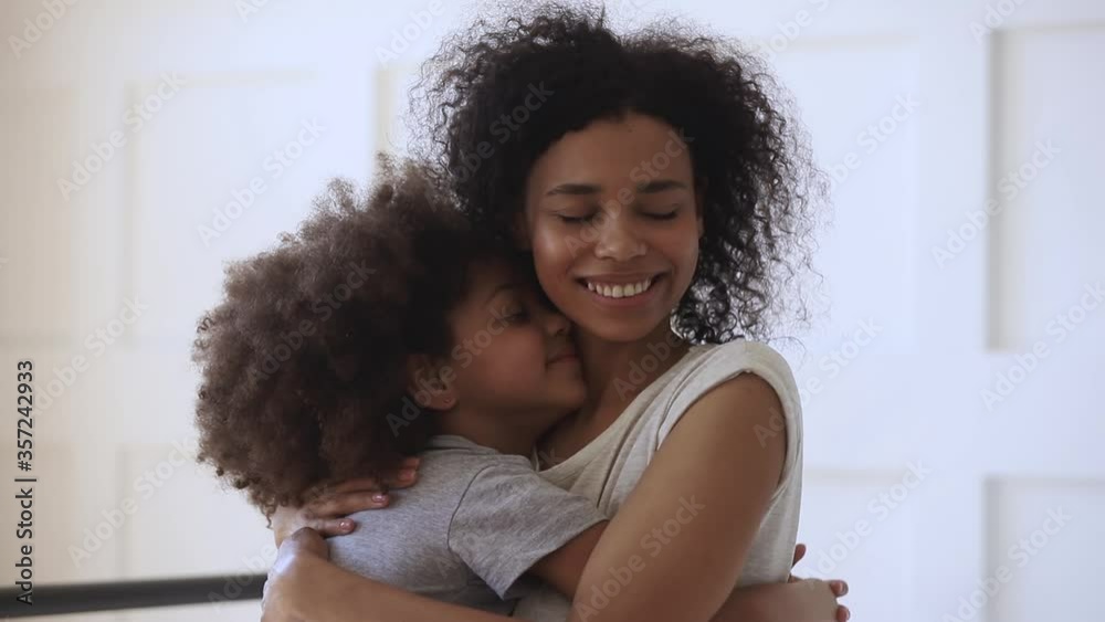 Happy loving young black mother hugging cute little child daughter holding tight cuddling looking, affectionate african american family mom foster parent embracing small kid girl bonding together