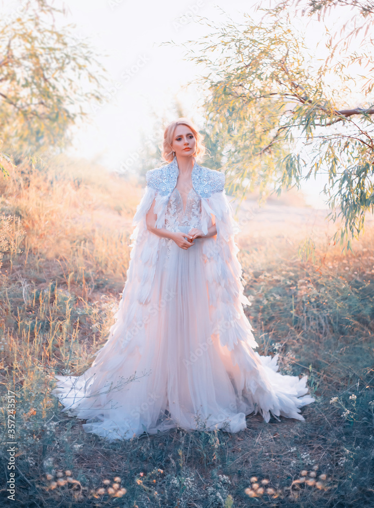 beautiful woman bride. Wedding trend creative coat, embroidered with silver stones bird feathers cape. White long evening romantic luxury dress. Fantasy Queen Elegant blonde hairstyle. autumn nature