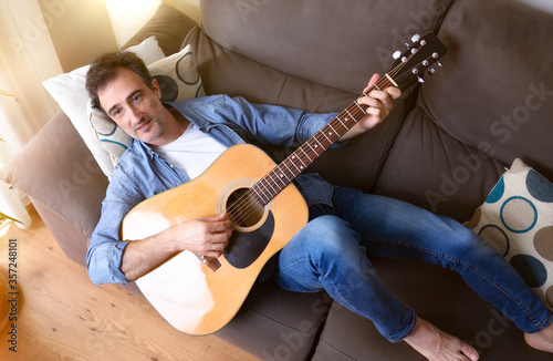 Man lying on sofa playing guitar at home top detail photo