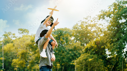 Lifestyle Asian family Father and son sat on his shoulders and run in  park. Paper plane as a toy in hand of kid And there are many big trees in garden Is natural in the morning of summer