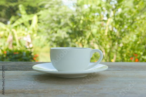 A cup of coffee on a wooden table on a bright sunny day with a nature background.