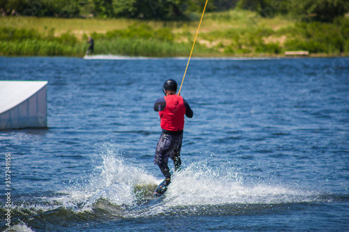 The man does wakeboarding on the water in the summer in a helmet and wetsuit. © Hennadii
