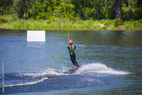 The man does wakeboarding on the water in the summer in a helmet and wetsuit.