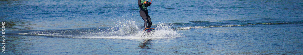 The man does wakeboarding on the water in the summer in a helmet and wetsuit. The man does wakeboarding on the water in the summer in a helmet and wetsuit.
