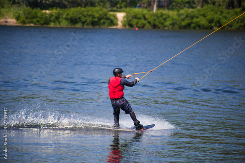 The man does wakeboarding on the water in the summer in a helmet and wetsuit. © Hennadii