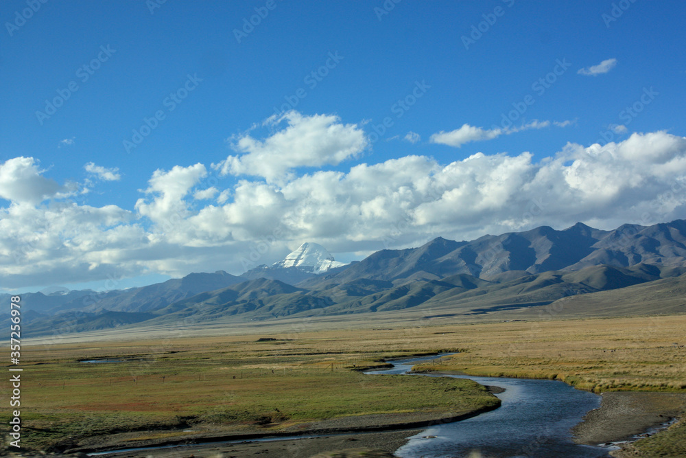 First view on Kailash Mountain rising from Barkha plain from the road from the distance with fields in front with river First view on Kailash Mountain rising from Barkha plain from the road from the distance with fields in front with river