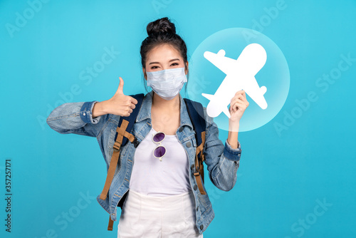 Portrait of young attractive asian girl wear and smile under mask show thumbs up and paper plane in bubble new normal traveler concept with low risk travel or ready to travel, fit for fly after reopen