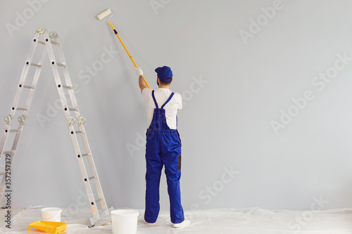 Fototapeta Naklejka Na Ścianę i Meble -  Worker painter paints a wall.Back view. Professional builder makes repairs.