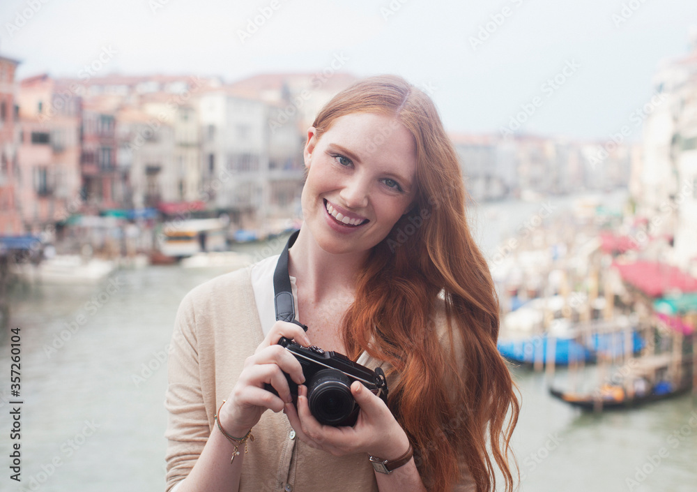 Portrait smiling woman holding digital camera at waterfront in Venice