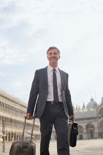 Smiling businessman pulling suitcase through Saint Mark's Square in Venice