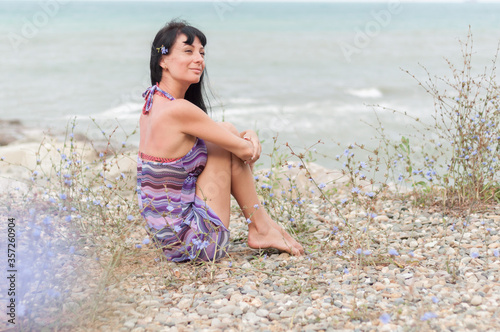 Beautiful brunette girl is sitting on the coast. The concept of vacation and travel to warm countries.