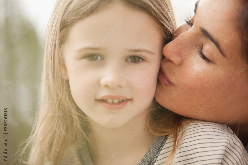 Close up portrait of mother kissing daughter’s cheek Close up portrait of mother kissing daughter’s cheek