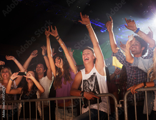 Enthusiastic crowd with arms raised behind railing at concert
