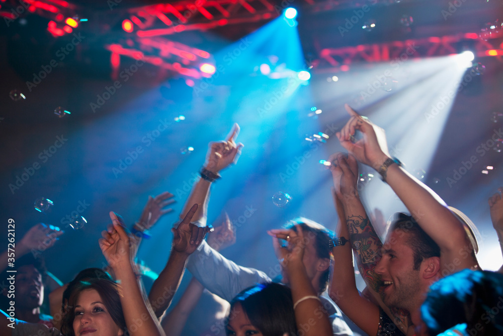 Enthusiastic crowd with arms raised on dance floor of nightclub