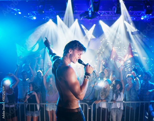 Bare chested singer performing on stage with crowd in background