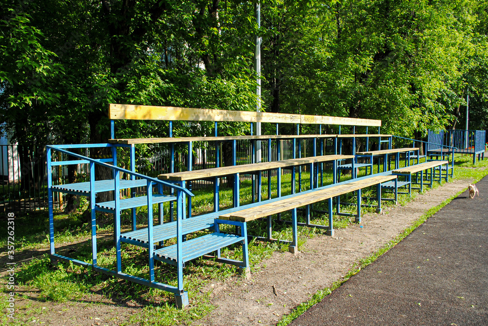 Empty spectator stand on an amateur soccer field. Wooden grandstand at the school stadium. Sports group games on an amateur level. Summer outdoor sports.