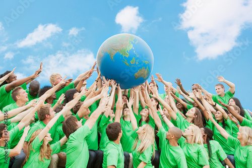 Fotografie Team in green t-shirts lifting globe overhead