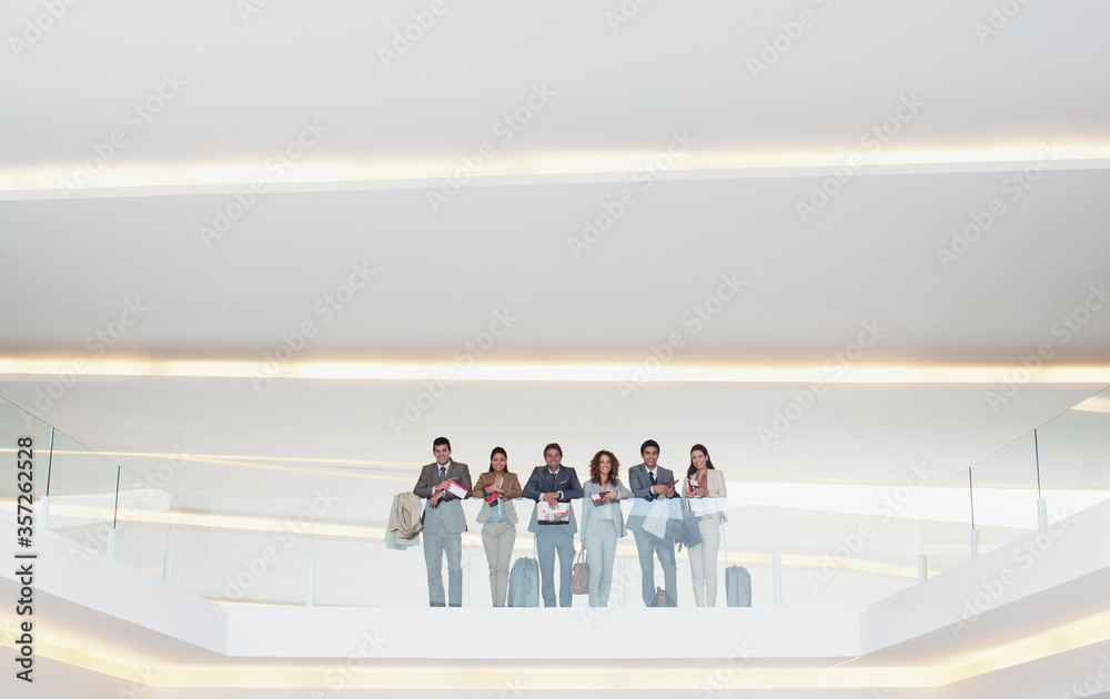 Portrait business people standing at glass balcony railing in modern office
