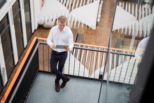 Businessman standing on gallery of modern office, using digita? tablet photo
