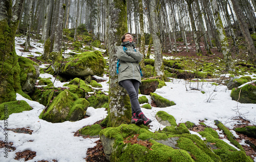 Woman leaning on beech tree in Northern Black Forest with snow remnants during springtime photo