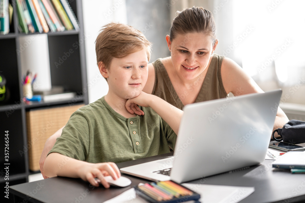 Mother homeschooling her son and using laptop at home Mother homeschooling her son and using laptop at home