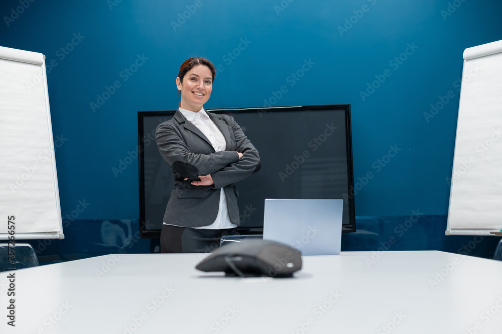 Friendly woman dressed in a suit conducts an online conversation on a laptop in a conference room. Female business coach conducts training. Remote negotiations in quarantine. Friendly woman dressed in a suit conducts an online conversation on a laptop in a conference room. Female business coach conducts training. Remote negotiations in quarantine.