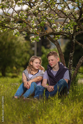 A young man and a girl sit under a blooming Apple tree © jura