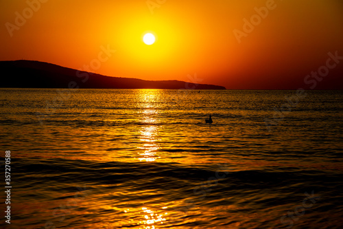Beautiful orange view at sunrise, of the calm sea and sea coast with hills in the distance