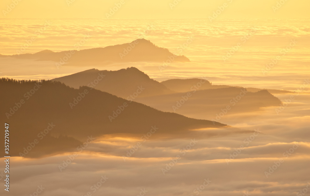 Aerial view of mountaintops over clouds at sunset