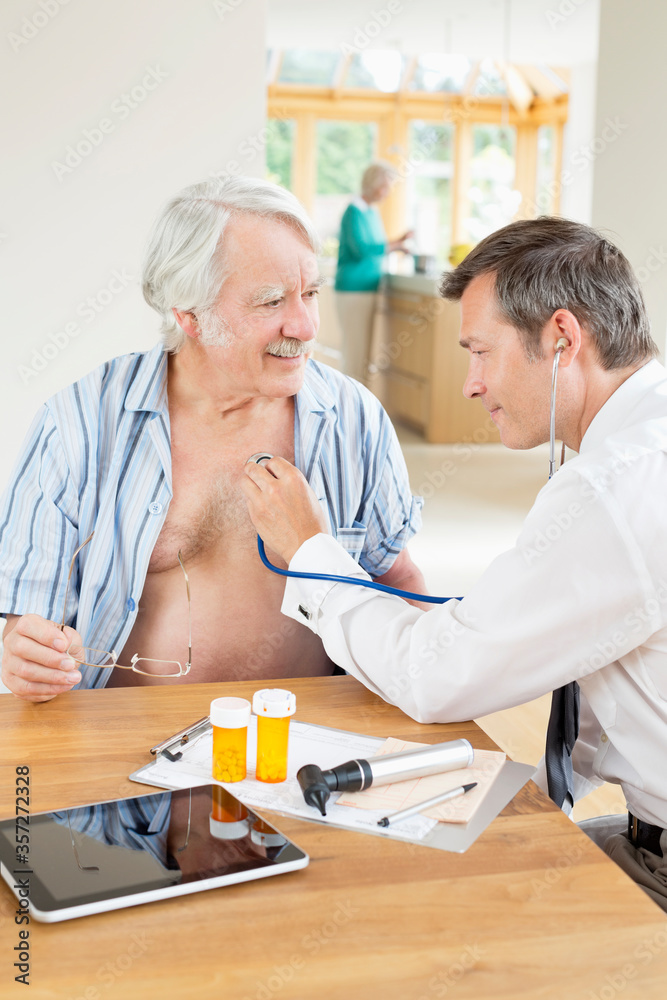 Obraz premium Doctor listening to older patient's heartbeat at house call