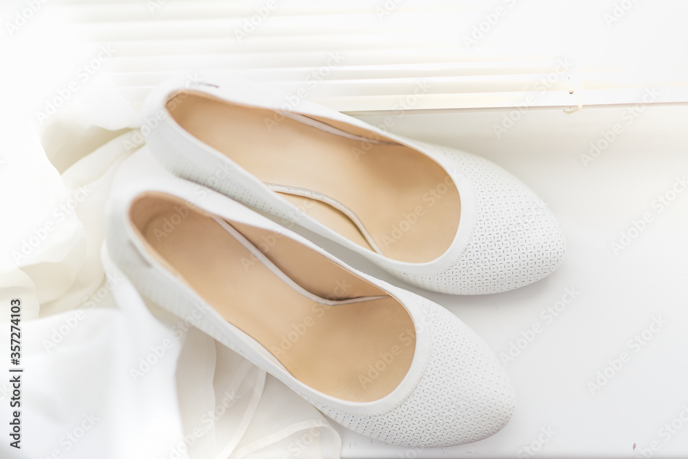white shoes for the bride on a background of a bright window with jalousie white shoes for the bride on a background of a bright window with jalousie