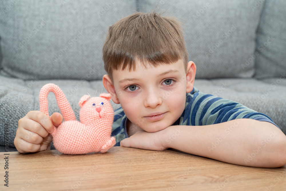 Cute child blond boy in casual clothes playing with handmade toy.