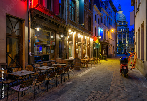 Fototapeta Naklejka Na Ścianę i Meble -  Old cozy narrow street with tables of restaurant in historic city center of Antwerpen (Antwerp), Belgium. Night cityscape of Antwerp. Architecture and landmark of Antwerpen