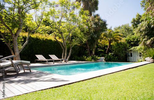 Murais de parede Lawn chairs and swimming pool in backyard