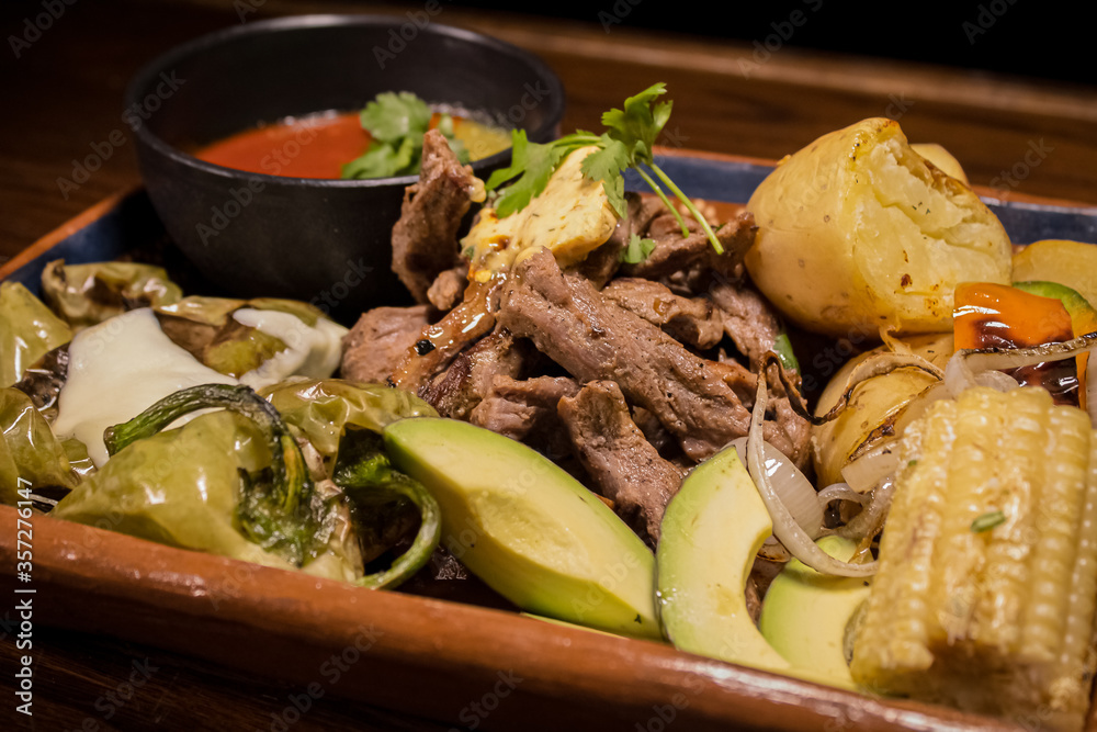 Carne asada servida con elote, aguacate, papas y salsas picantes