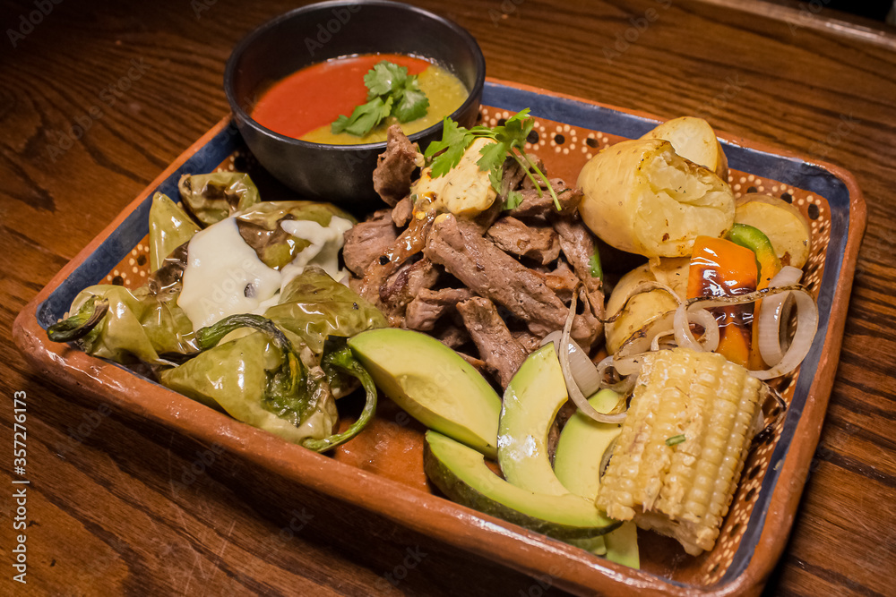 Carne asada servida con elote, aguacate, papas y salsas picantes