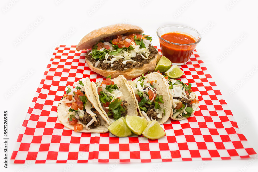 Tacos y tortas de barbacoa sobre mantel de cuadros rojos y fondo blanco