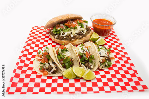 Tacos y tortas de barbacoa sobre mantel de cuadros rojos y fondo blanco