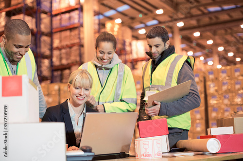 Businesswoman and workers using laptop in warehouse
