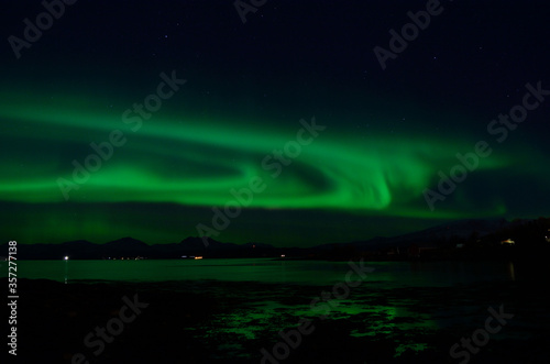 strong aurora borealis on autumn sky with reflection in cold autumn fjord